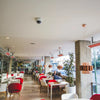 Bright café interior with Bromic Heating Tungsten Electric Smart-Heat white heaters mounted along the ceiling, keeping guests comfortably warm while dining at modern red and white tables.