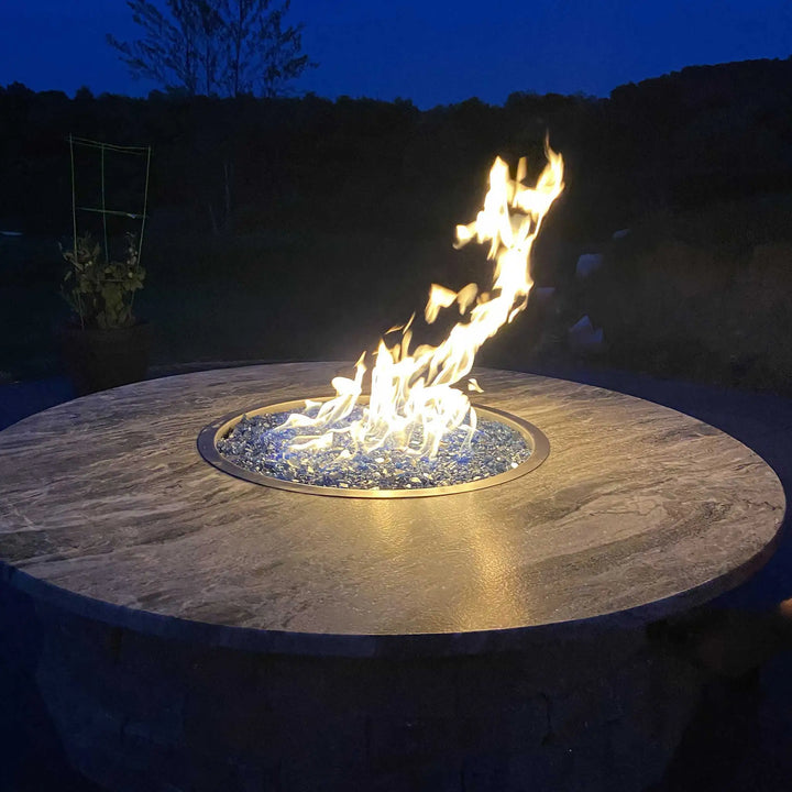 Round outdoor fire pit with blue fire glass, illuminated at night against a dark sky, creating a warm and inviting outdoor ambiance