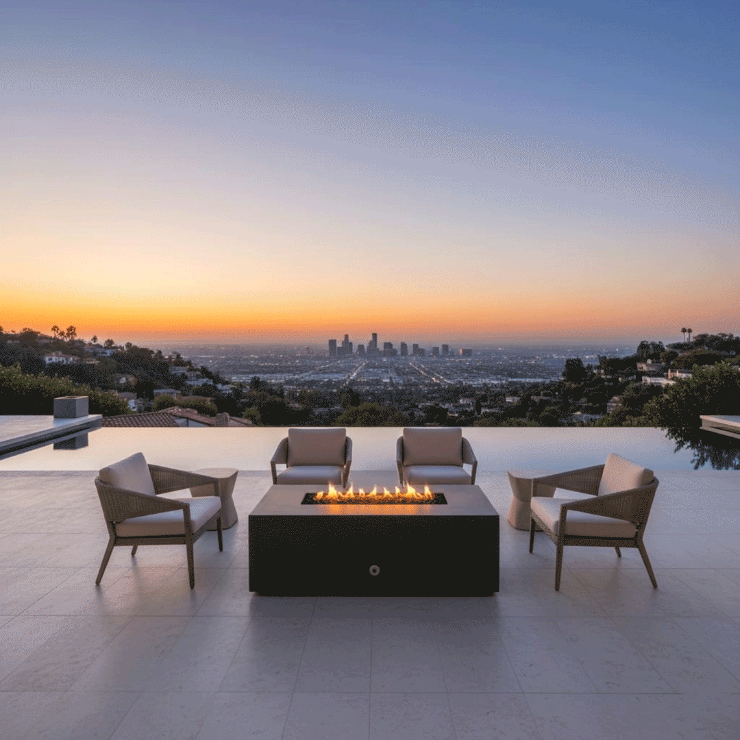A modern fire pit with a rectangular graphite profile sits centrally on a tiled terrace overlooking a sprawling city skyline at twilight. Four woven armchairs surround the fire feature, offering a front-row view of the sunset and urban lights. The steady amber flames of the gas fire pit reflect softly on the adjacent infinity pool, establishing a serene backyard oasis that blends architectural design with panoramic views.