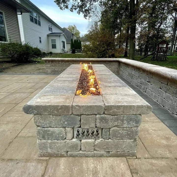 Backyard patio fire feature built from rustic stone with a long, glowing flame display powered by the HPC Fire Inspired Linear Flat Torpedo T-Burner, creating warmth and charm for gatherings.
