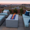 Contemporary outdoor seating area with modern gray furniture and a fire table glowing with blue fire glass, powered by the HPC Fire Inspired Linear Flat Torpedo T-Burner.