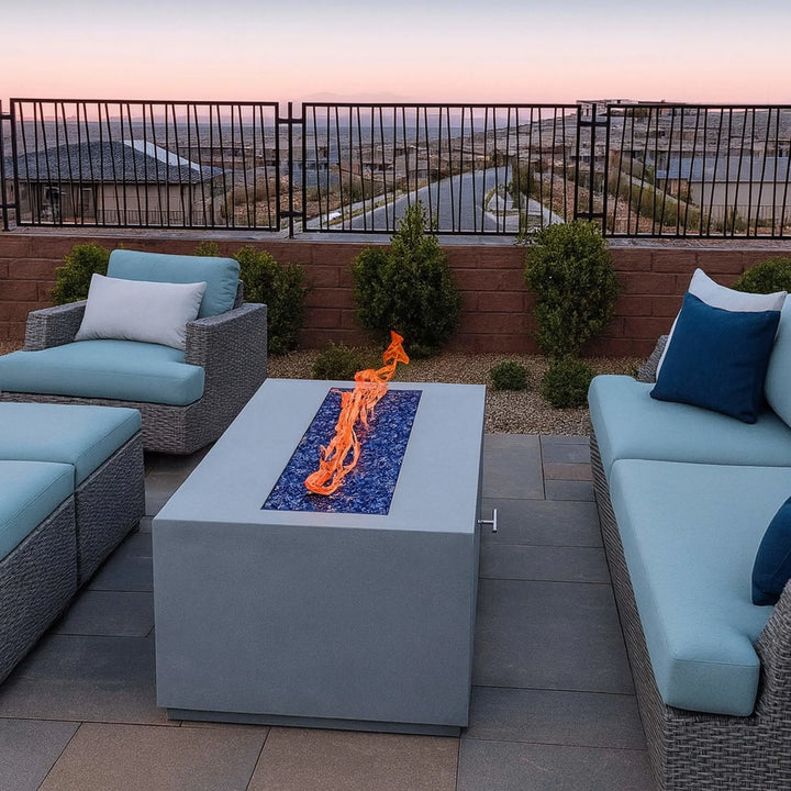 Contemporary outdoor seating area with modern gray furniture and a fire table glowing with blue fire glass, powered by the HPC Fire Inspired Linear Flat Torpedo T-Burner.