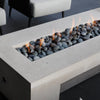 Minimalist rectangular concrete fire table with smooth river stones and gentle flames from the HPC Fire Inspired Linear Flat Torpedo T-Burner, adding elegance to a modern patio setting.