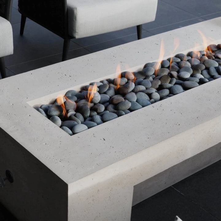 Minimalist rectangular concrete fire table with smooth river stones and gentle flames from the HPC Fire Inspired Linear Flat Torpedo T-Burner, adding elegance to a modern patio setting.