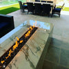 Modern covered patio with a luxurious marble fire table by the pool, powered by the HPC Fire Inspired Linear Flat Torpedo T-Burner with glowing flames reflecting off the polished surface.
