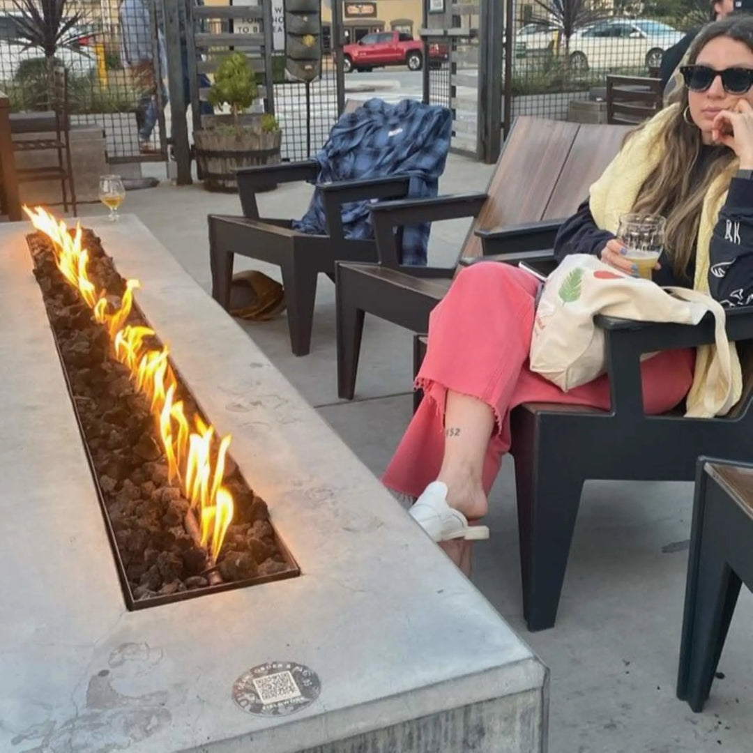 Contemporary lounge featuring a long linear fire pit lined with decorative glass media and surrounded by industrial-style metal framework, fueled by the HPC Fire Inspired Linear Interlink Torpedo T-Burner.