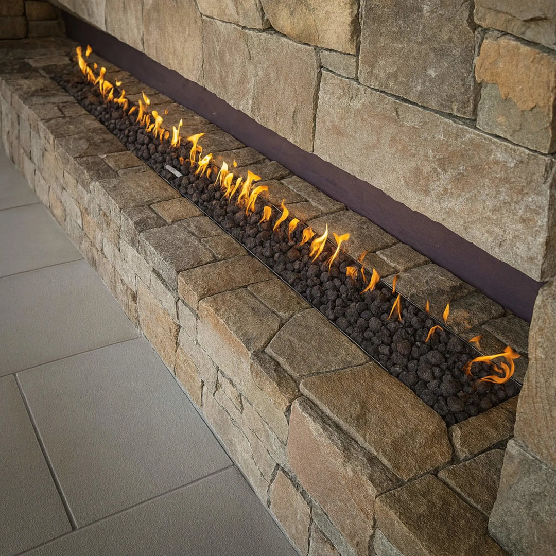 Outdoor patio setting with guests enjoying drinks around a concrete linear fire table featuring bright, even flames from the HPC Fire Inspired Linear Interlink Torpedo T-Burner.