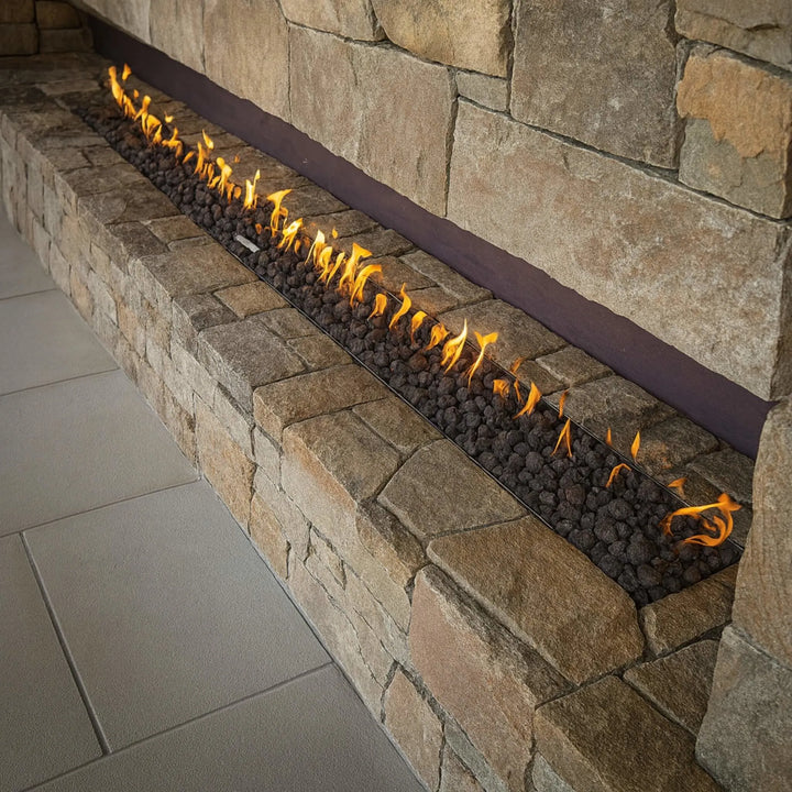 Outdoor patio setting with guests enjoying drinks around a concrete linear fire table featuring bright, even flames from the HPC Fire Inspired Linear Interlink Torpedo T-Burner.