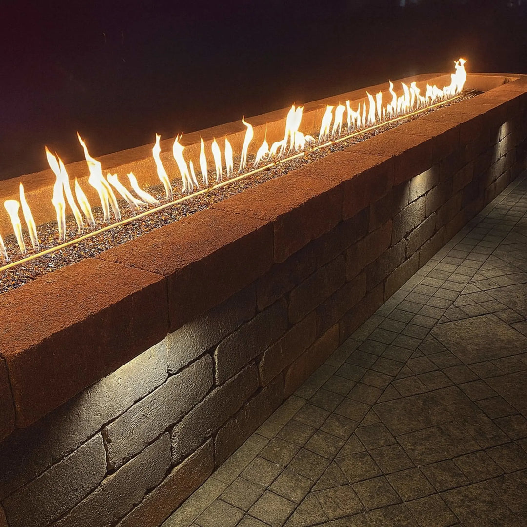 Rustic stone fire feature built into a wall, producing a clean line of flames across lava rock media, powered by the durable HPC Fire Inspired Linear Interlink Torpedo T-Burner.