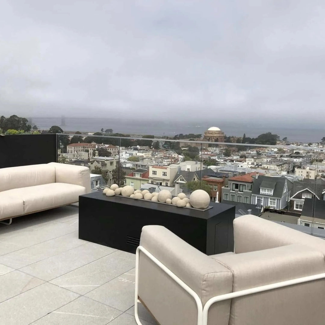 Elegant rooftop patio with a black rectangular fire feature filled with decorative spheres, offering a panoramic view of the city, highlighting the modern style of the HPC Fire Inspired Torpedo T-Burner in a linear trough design.