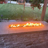 Contemporary backyard with a rectangular stone fire pit glowing with warm orange flames at dusk,  a perfect showcase of the HPC Fire Inspired Linear Trough Drop-In Torpedo T-Burner ambiance.