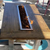 Custom-built wooden fire table with a rectangular inset burner filled with lava rock, powered by the HPC Fire Inspired Linear Trough Drop-In Torpedo T-Burner, ideal for patio or deck relaxation.