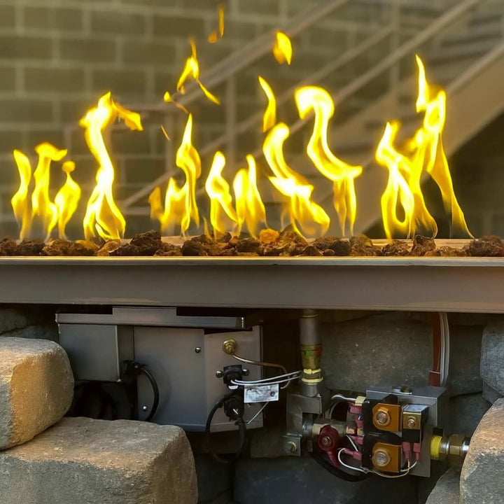 Close-up of the HPC Fire Inspired Linear Trough Drop-In Torpedo T-Burner installed in a stone enclosure, showing bright yellow flames and professional-grade components beneath for reliable outdoor performance.