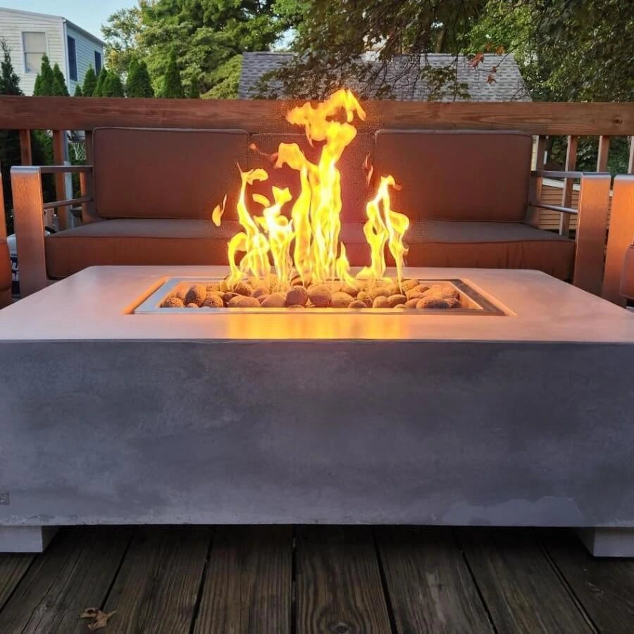 Modern deck setting featuring the Hearth Products Controls (HPC) Fire Inspired Rectangle Drop-In Burner, beautifully integrated into a sleek concrete fire table. The burner is filled with smooth fire stones, producing tall, vibrant flames that add warmth and ambiance—perfectly complementing the surrounding contemporary outdoor furniture and cozy seating area.