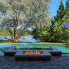 Modern lakeside patio design featuring a recessed rectangular HPC Fire Inspired burner built into stone pavers, creating a luxurious fire feature with a peaceful water and tree backdrop.