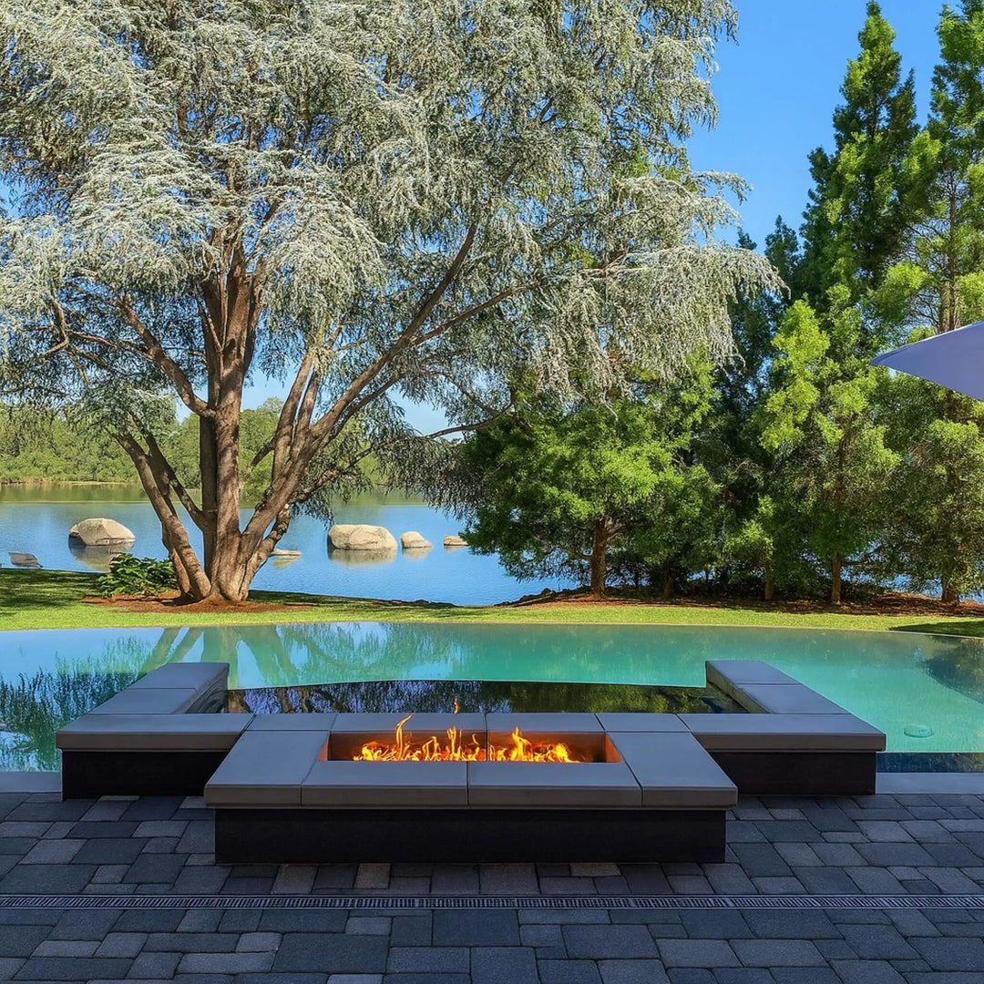 Modern lakeside patio design featuring a recessed rectangular HPC Fire Inspired burner built into stone pavers, creating a luxurious fire feature with a peaceful water and tree backdrop.