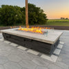 Contemporary outdoor fire feature showcasing an HPC Fire Inspired rectangular drop-in burner with a glass wind guard, built into a stone fire pit surrounded by open fields at sunset.