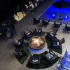 Evening view of a circular fire pit with HPC Torpedo Penta burner, illuminating a poolside hotel lounge area surrounded by modern Adirondack chairs and dramatic night lighting.