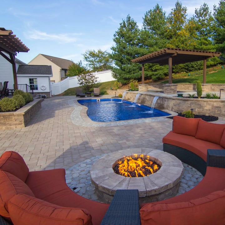 Built-in round fire pit powered by a Penta burner, situated near a luxury backyard pool with cascading waterfalls, curved seating, and elegant paver hardscape for the ultimate outdoor retreat.