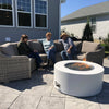 A contemporary white round fire pit with glass media is the center of a friendly backyard conversation, illustrating the perfect fire feature for patios and gatherings.