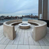 Modern rooftop patio fire pit with a city skyline in the background, featuring a clean Penta burner pan ready for ignition, surrounded by smooth stone seating.