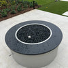 Sleek round fire pit with black granite top and wet reflective black fire glass, displaying HPC’s stainless steel drop-in burner ring in an elegant outdoor setting.