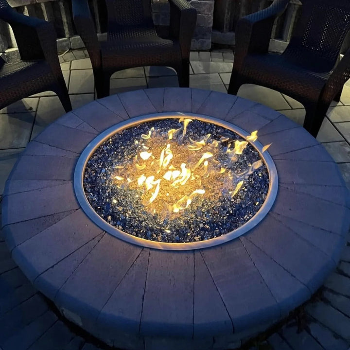 A glowing round fire pit filled with shimmering blue fire glass on a stone paver base, surrounded by chairs for cozy evening relaxation under the stars.