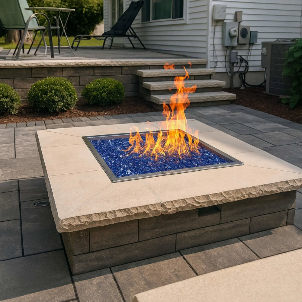 A modern patio fire pit installation showcases a square drop-in burner pan filled with vibrant blue fire glass, delivering brilliant flame patterns and sleek, contemporary charm.