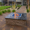 Outdoor fire feature set in a stone-top pit with a Square Drop-In Penta Burner by HPC Fire, producing lively flames over cobalt blue fire glass—perfect for upscale residential landscapes.