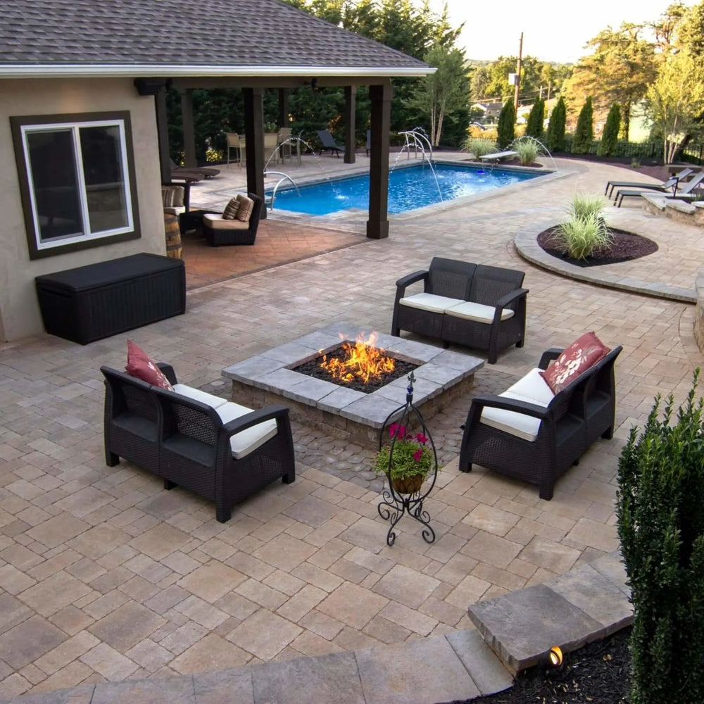 Cozy outdoor lounge setup featuring a lit square fire pit surrounded by wicker furniture and poolside elegance, showcasing the welcoming glow of an HPC square flat burner for family gatherings.