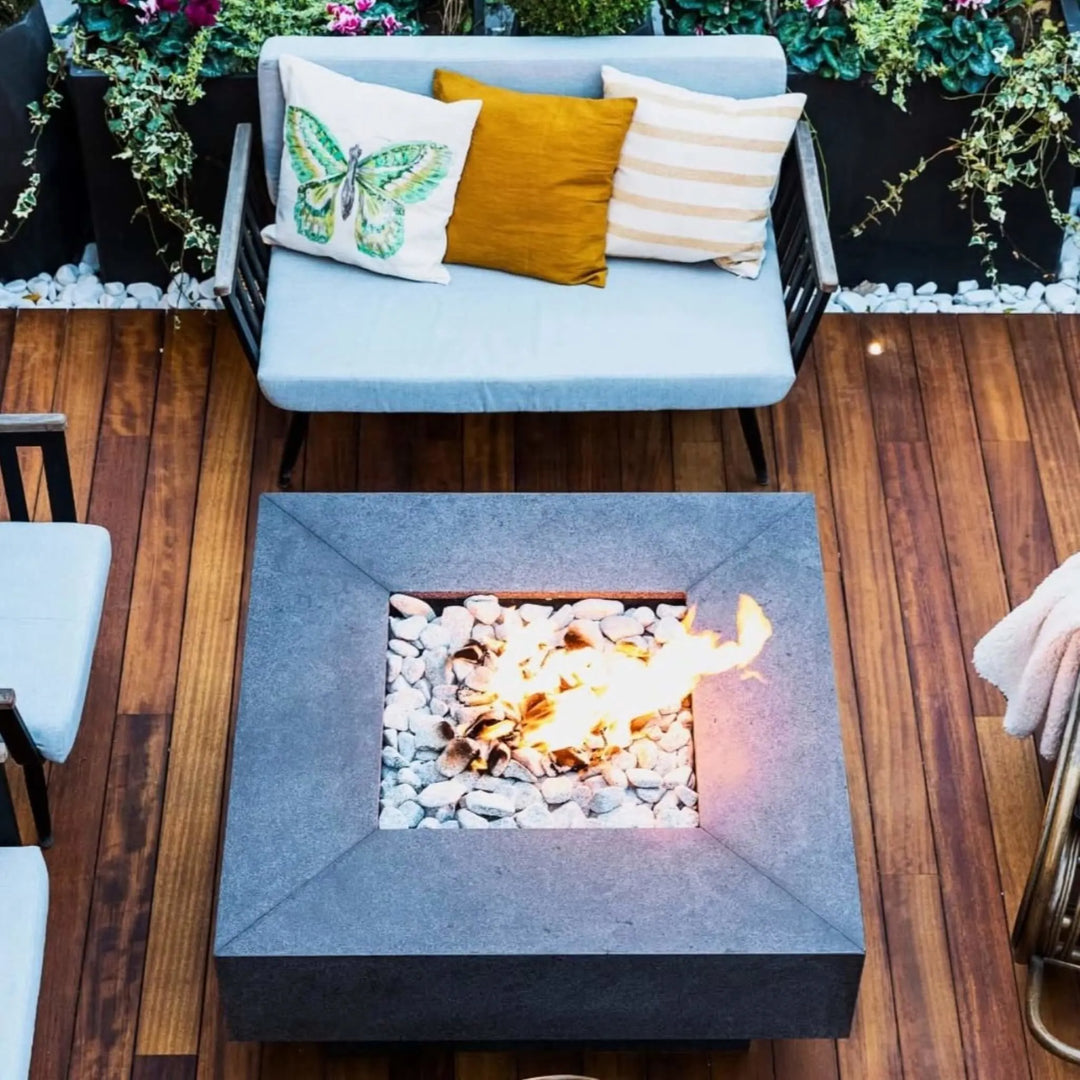 Charming rooftop or patio deck showcasing a dark textured concrete fire pit with an HPC flat burner / bright flame rising through white stone media, creating a cozy vibe in a compact, stylish outdoor space.