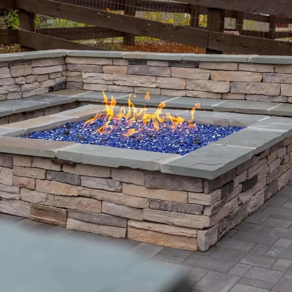 Built-in stone fire feature with vivid cobalt blue fire glass and bold yellow-orange flames, featuring HPC’s square flat burner technology / perfectly nestled into a wrap-around seating wall for social evenings.