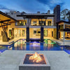 Ultra-modern luxury home with glowing square fire pit at the heart of the pool deck / blue fire glass and HPC Fire square flat burner create a stunning flame effect framed by contemporary architecture.