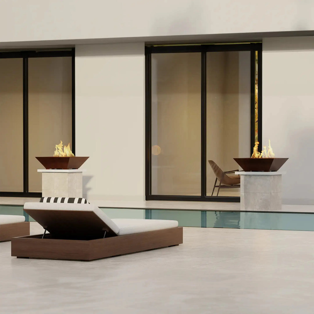 Plaza Moreno 29-inch square copper fire bowls, elegantly placed on pedestals by a modern poolside, creating a luxurious ambiance with their sleek design and vibrant flames. Ideal for upscale outdoor living spaces, combining style and functionality