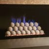 Modern fireplace burner setup with stacked natural gray ceramic fireballs glowing softly over a custom pan burner, producing vibrant blue flames with subtle golden tips. A contemporary, clean look ideal for luxury gas fireplaces and minimalist interiors.