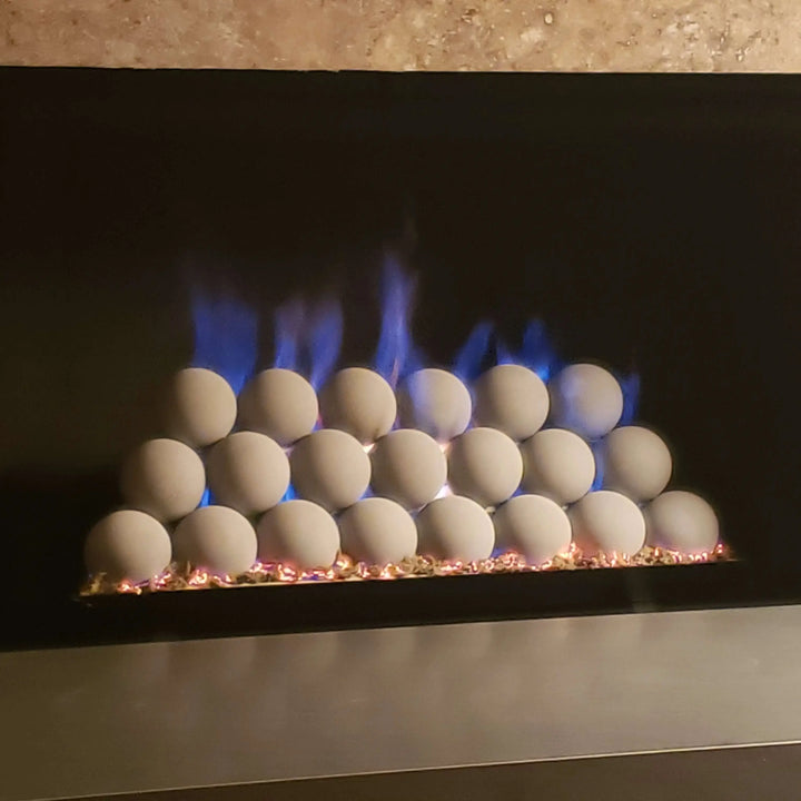 Modern fireplace burner setup with stacked natural gray ceramic fireballs glowing softly over a custom pan burner, producing vibrant blue flames with subtle golden tips. A contemporary, clean look ideal for luxury gas fireplaces and minimalist interiors.
