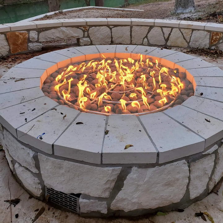 Beautifully built-in stone fire pit featuring the Starfire Designs 36-inch fire pit ring burner with vibrant, full flames dancing over lava rock. Surrounded by a stylish light-colored stone coping and integrated venting panel for proper airflow, this outdoor gas fire pit is the perfect backyard centerpiece for cozy evenings and gatherings.