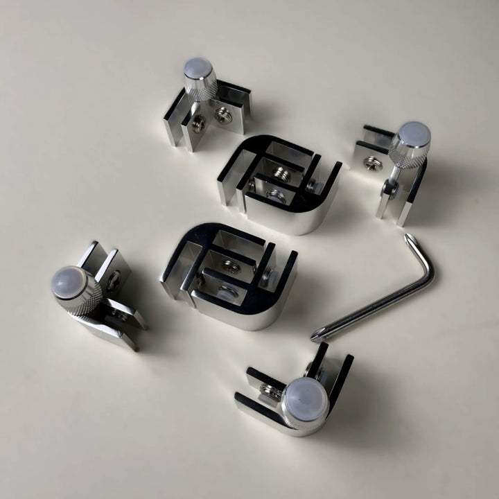 Top view of the Starfire Designs Béton Fire Pit Replacement Glass Wind Guard Clips Kit featuring precision-milled L-shaped clips, mounting hardware, and adjustment tools for rectangular or square guards.