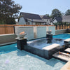A modern backyard pool featuring The Outdoor Plus Cazo Fire and Water Bowl in Rustic White GFRC, elegantly displayed on raised pillars with fire and cascading water elements. The dual bowls create a stunning focal point, blending warm flames and gentle water flow above a luxurious black tile spa. Surrounded by a crystal-clear pool, light stone walls, and tropical greenery, this space offers a serene and stylish outdoor escape in a contemporary residential setting.