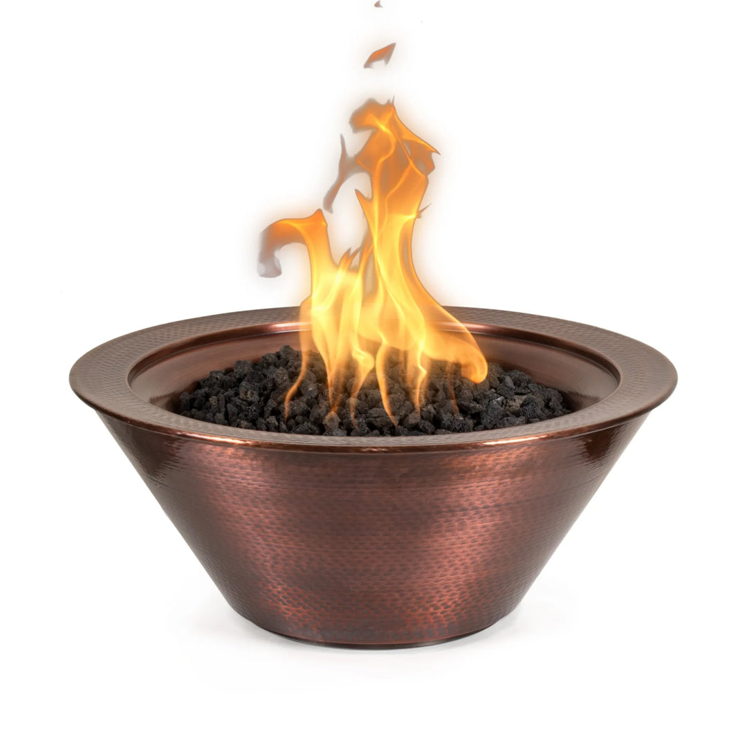 Hand-hammered copper Cazo fire bowl with a warm, glowing flame rising from a bed of black lava rock. This round gas fire feature showcases artisan craftsmanship and timeless elegance—perfect for upscale outdoor living spaces.