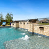 A luxurious backyard pool featuring multiple Maya Fire and Water Bowls by The Outdoor Plus in a modern Chocolate finish. Mounted on a beautifully crafted natural stone wall, each bowl spills a steady stream of water into the sparkling blue pool below. Bubblers and lounge seating in the shallow tanning ledge create a serene and resort-style atmosphere perfect for outdoor relaxation and upscale design.
