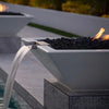 A close-up of The Outdoor Plus Maya Fire and Water Bowl in a crisp Limestone finish, showcasing flickering flames above dark lava rocks. A smooth sheet of water spills cleanly into the pool below, creating a modern, minimalist focal point for any contemporary outdoor space or luxury pool environment.