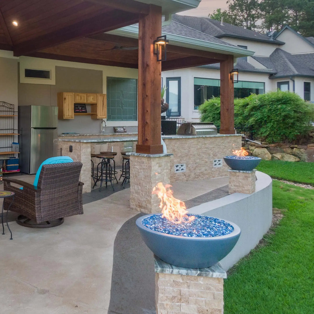 Gray concrete Sedona Fire Bowls filled with blue fire glass installed across a wraparound patio, perfect for lakeside lounging and entertaining in style.