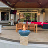 Three gray Sedona Fire Bowls with vibrant blue fire glass lined along a luxury backyard patio, casting warm flames across the outdoor dining and lounge areas at sunset.