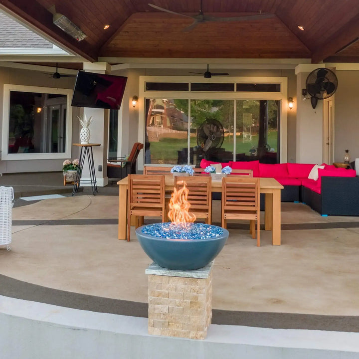 Three gray Sedona Fire Bowls with vibrant blue fire glass lined along a luxury backyard patio, casting warm flames across the outdoor dining and lounge areas at sunset.