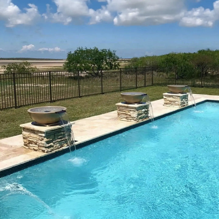 Three brown Sedona water bowls with copper scuppers, mounted on stacked stone bases, gently pouring streams into a bright blue pool for a resort-style backyard design.