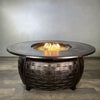 Golden Flame Bel Air 48” Oval Cast Aluminum Natural Gas Fire Table illuminated with golden flames, enhanced by a glass wind guard and dazzling fire glass.