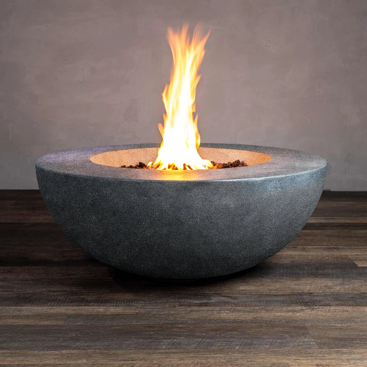 A front view of the Beton 42" Graphite Round Concrete Natural Gas Fire Pit showcasing a sleek, round bowl design with a wide surface area. The fire pit contains black lava rocks and produces a strong, even flame through the push-button ignition system, ideal for outdoor fire pit gatherings and creating a modern outdoor ambiance.