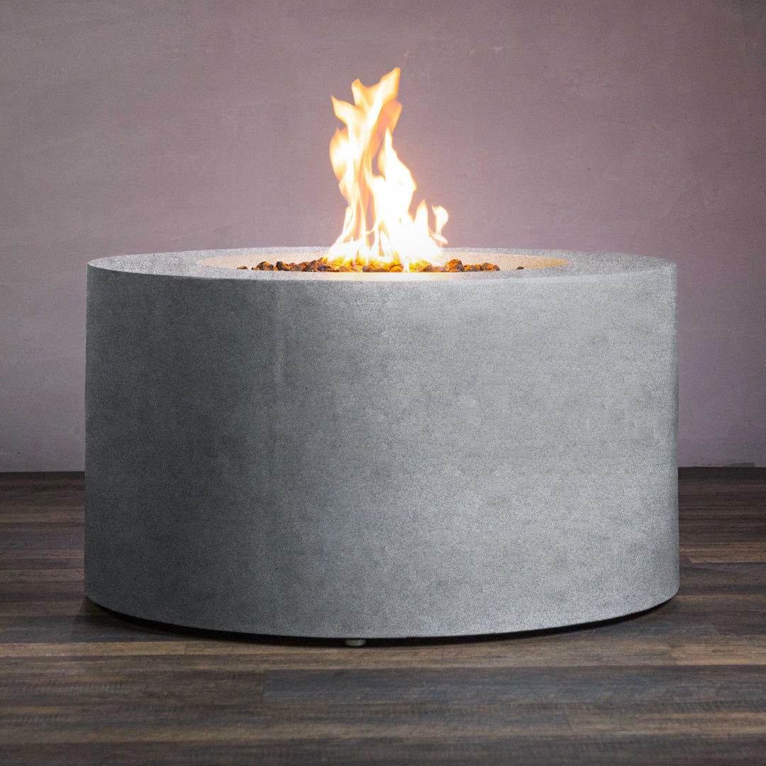 Side view of the Beton 42-inch natural gray round concrete gas fire pit with access door. The clean and simple cylindrical design enhances any outdoor setting. Made from high-quality concrete, this natural gas fire pit is both durable and stylish. The built-in access door for the propane tank adds convenience while maintaining a sleek appearance, making it perfect for luxury outdoor living spaces and backyard fire pits.