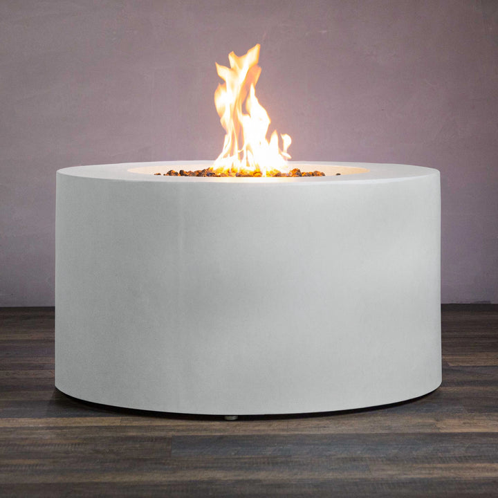 Side view of the Beton 42-inch white round concrete gas fire pit with access door, displaying a consistent and even flame. The durable white concrete body contrasts beautifully with the warm glow of the fire, perfect for outdoor patios or gardens looking for a modern fire feature